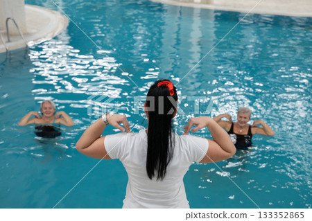 Instructor leading aquatic fitness training for group senior women in a swimming pool. Concept of health, exercise, wellness, water therapy, and active aging lifestyle 133352865