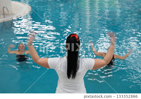 Instructor leading aquatic fitness training for group senior women in a swimming pool. Concept of health, exercise, wellness, water therapy, and active aging lifestyle Instructor leading aquatic fitness training for group senior women in a swimming pool. Concept of health, exercise, wellness, water therapy, and active aging lifestyle 133352866