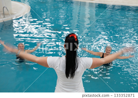 Instructor leading aquatic fitness training for group senior women in a swimming pool. Concept of health, exercise, wellness, water therapy, and active aging lifestyle 133352871