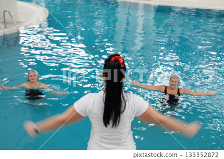 Instructor leading aquatic fitness training for group senior women in a swimming pool. Concept of health, exercise, wellness, water therapy, and active aging lifestyle 133352872