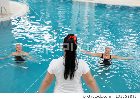 Instructor leading aquatic fitness training for group senior women in a swimming pool. Concept of health, exercise, wellness, water therapy, and active aging lifestyle 133352885