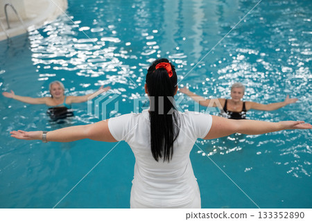 Instructor leading aquatic fitness training for two senior women in a swimming pool. Concept of health, exercise, wellness, water therapy, and active aging lifestyle. 133352890