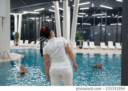Instructor leading aquatic fitness training for group senior women in a swimming pool. Concept of health, exercise, wellness, water therapy, and active aging lifestyle Instructor leading aquatic fitness training for group senior women in a swimming pool. Concept of health, exercise, wellness, water therapy, and active aging lifestyle 133352894