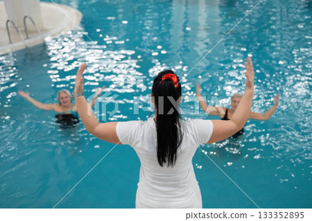 Instructor leading aquatic fitness training for group senior women in a swimming pool. Concept of health, exercise, wellness, water therapy, and active aging lifestyle Instructor leading aquatic fitness training for group senior women in a swimming pool. Concept of health, exercise, wellness, water therapy, and active aging lifestyle 133352895