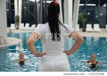 Instructor leading aquatic fitness training for group senior women in a swimming pool. Concept of health, exercise, wellness, water therapy, and active aging lifestyle Instructor leading aquatic fitness training for group senior women in a swimming pool. Concept of health, exercise, wellness, water therapy, and active aging lifestyle 133352896