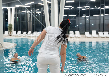 Instructor leading aquatic fitness training for group senior women in a swimming pool. Concept of health, exercise, wellness, water therapy, and active aging lifestyle Instructor leading aquatic fitness training for group senior women in a swimming pool. Concept of health, exercise, wellness, water therapy, and active aging lifestyle 133352897