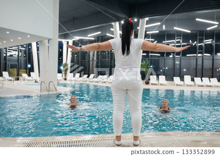 Instructor leading aquatic fitness training for group senior women in a swimming pool. Concept of health, exercise, wellness, water therapy, and active aging lifestyle 133352899