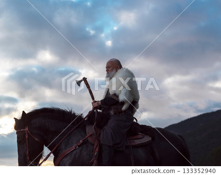 A fierce Viking warrior on horseback, wielding an axe, stands against a dramatic sunset sky with clouds and mountains, embodying strength, exploration, and ancient legend. A fierce Viking warrior on horseback, wielding an axe, stands against a dramatic sunset sky with clouds and mountains, embodying strength, exploration, and ancient legend. 133352940