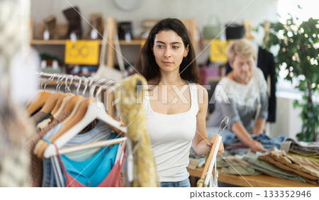 Woman choosing ribbon clothes against the background of a customer in a store Woman choosing ribbon clothes against the background of a customer in a store 133352946