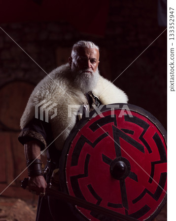 A resolute Viking chieftain, with a white beard and a fur cloak, stands, holding a large sword and a red and black round shield, embodying strength, security, and protection in ancient resolve. A resolute Viking chieftain, with a white beard and a fur cloak, stands, holding a large sword and a red and black round shield, embodying strength, security, and protection in ancient resolve. 133352947
