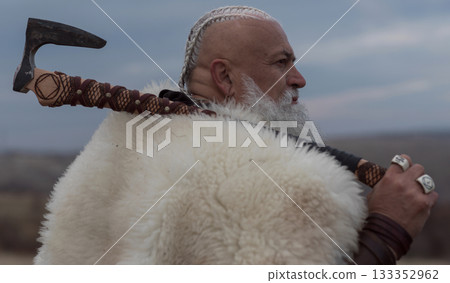 Viking warrior with axe standing on mountain cliff, wearing fur cloak and leather armor, overlooking dramatic landscape. Historical Nordic fighter Viking warrior with axe standing on mountain cliff, wearing fur cloak and leather armor, overlooking dramatic landscape. Historical Nordic fighter 133352962