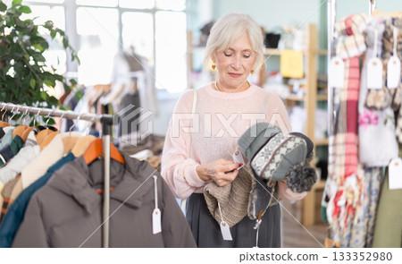 Focused european mature woman choose hat for winter season in clothing outlet store 133352980