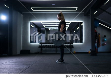 Strong woman lifting weights in a modern gym during an intense workout session in the evening Strong woman lifting weights in a modern gym during an intense workout session in the evening 133353006