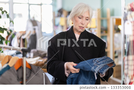 Mature woman chooses jeans trousers in clothing store Mature woman chooses jeans trousers in clothing store 133353008
