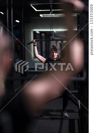 Woman lifting weights in a gym during a focused workout session with equipment and trainers in the background 133353009