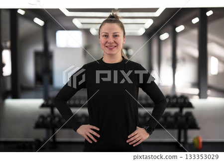 Smiling woman stands confidently with hands on hips in modern gym setting during workout session Smiling woman stands confidently with hands on hips in modern gym setting during workout session 133353029
