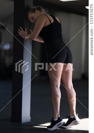 Woman stretching against a pole in a gym during a fitness routine in early morning light 133353079