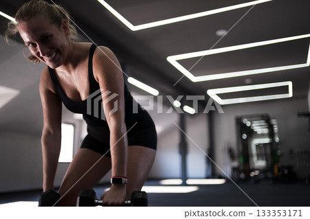 Woman lifting weights in modern gym with bright lighting during fitness session 133353171