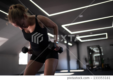 Fitness enthusiast performs strength training with dumbbells in a modern gym during daytime 133353181