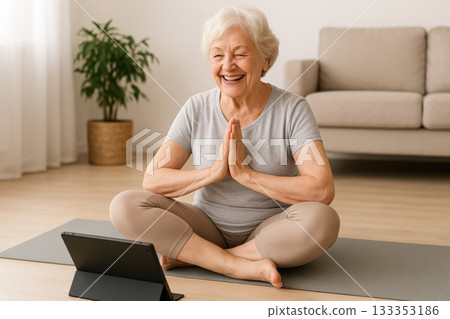 Elderly woman practices yoga in her living room while following an online class on her tablet in the morning light 133353186