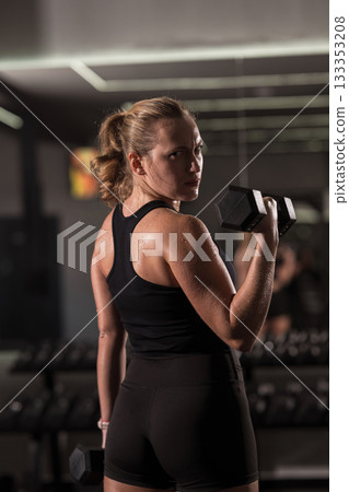 Woman lifting dumbbells in a modern gym focusing on fitness and strength training 133353208