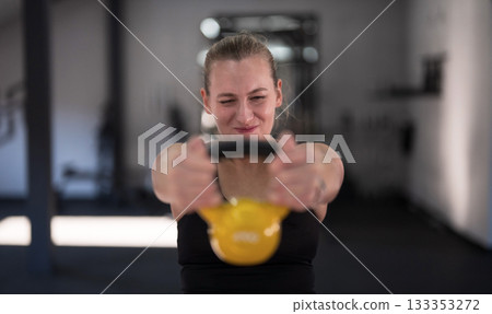 Young woman training with kettlebell in gym focused on fitness and strength building in morning hours Young woman training with kettlebell in gym focused on fitness and strength building in morning hours 133353272
