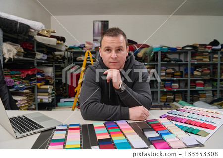 Tailor or designer with fabric swatches and laptop in studio, man thinking about color palette, fashion designer at work, textile industry, small business owner concept. 133353308