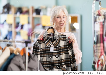 Mature woman chooses fashionable coat or jacket in clothing store 133353336