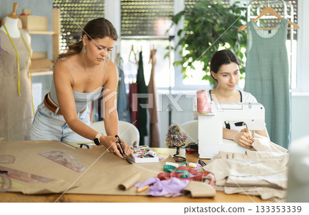 Female dressmaker cutting paper next to assistant Female dressmaker cutting paper next to assistant 133353339