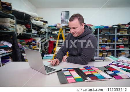 Fashion designer using laptop with fabric swatches in textile warehouse, designer working on color palettes, material selection, online order, small business owner, entrepreneur. Fashion designer using laptop with fabric swatches in textile warehouse, designer working on color palettes, material selection, online order, small business owner, entrepreneur. 133353342