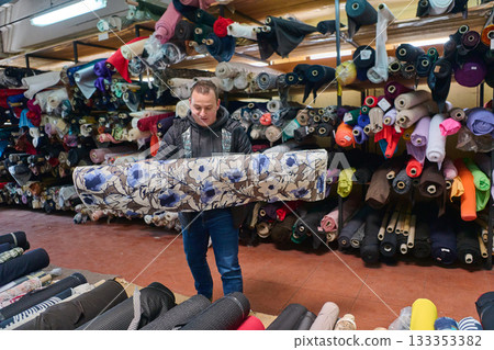 Designer carrying floral fabric roll in warehouse, surrounded by textiles, fabric store, textile industry, material selection, fabric rolls, textile production, designer choice. Designer carrying floral fabric roll in warehouse, surrounded by textiles, fabric store, textile industry, material selection, fabric rolls, textile production, designer choice. 133353382