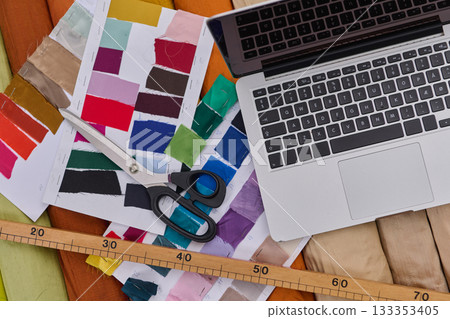 Fashion designer's workspace with laptop, color swatches, scissors, measuring tape, and fabric, design studio, creative process, product photo, mockup background. Fashion designer's workspace with laptop, color swatches, scissors, measuring tape, and fabric, design studio, creative process, product photo, mockup background. 133353405