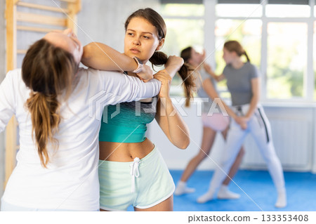 Teenage girl practicing close combat techniques in sparring during self-defence class Teenage girl practicing close combat techniques in sparring during self-defence class 133353408