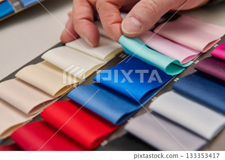 Hand selecting colorful fabric swatches, product photo, studio shot, clean studio background, textile samples for fashion design, material selection, copy space minimal background. 133353417