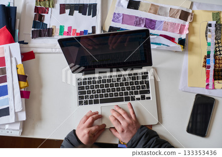 Fashion designer working on laptop surrounded by fabric swatches, creating new collection, top view, fashion industry concept, design process, creative workspace Fashion designer working on laptop surrounded by fabric swatches, creating new collection, top view, fashion industry concept, design process, creative workspace 133353436