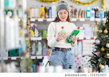 Young girl choosing dishwashing liquid in store with New Year decoration Young girl choosing dishwashing liquid in store with New Year decoration 133353437