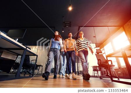 Group of young business team walking together through a modern office hallway, smiling and discussing work. Concept of confidence, teamwork, leadership, and positive workplace culture. Group of young business team walking together through a modern office hallway, smiling and discussing work. Concept of confidence, teamwork, leadership, and positive workplace culture. 133353464