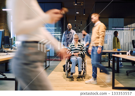 Diverse group of coworkers in a modern office, including a woman in a wheelchair being assisted by a colleague, symbolizing workplace inclusion, accessibility, and teamwork. Diverse group of coworkers in a modern office, including a woman in a wheelchair being assisted by a colleague, symbolizing workplace inclusion, accessibility, and teamwork. 133353557