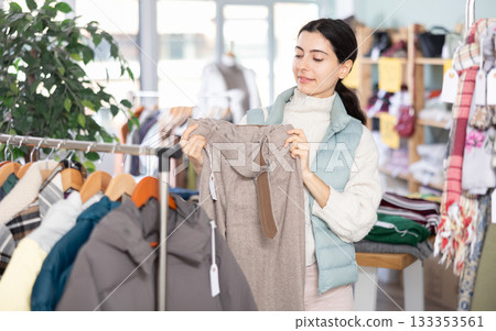 Focused young girl client selecting trousers in clothing shop. Winter clothing collection 133353561