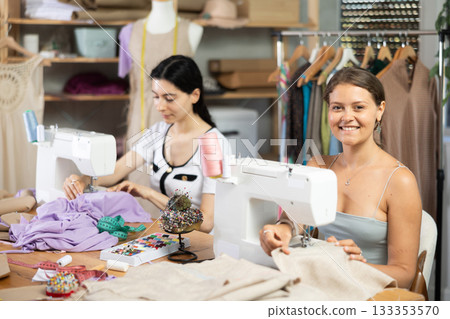 Female dressmakers stitching at machines in sewing workshop 133353570