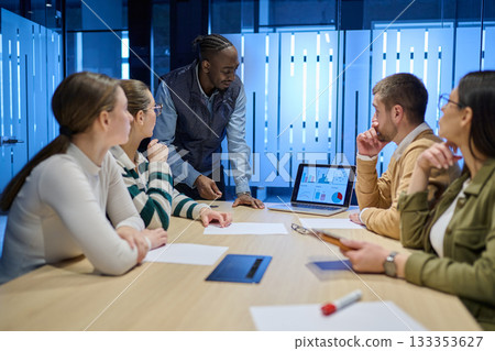 Diverse business team gathered around a table discussing analytics during a meeting in a modern office. Laptop screen shows charts and graphs, symbolizing teamwork, communication, and data driven 133353627
