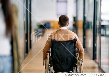 Confident businessman in a wheelchair moving independently through a modern office corridor, symbolizing accessibility, inclusion, and determination in the workplace. 133353642