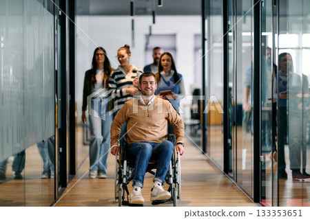 Group of diverse business people walking together in a modern office hallway, led by a confident smiling man in a wheelchair, representing inclusion, equality, and teamwork. 133353651