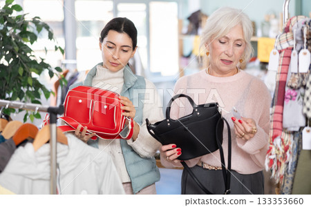 Elderly mother and her adult daughter choose together fashionable handbags in clothing store Elderly mother and her adult daughter choose together fashionable handbags in clothing store 133353660