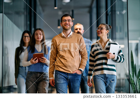 Group of young business team walking together through a modern office hallway, smiling and discussing work. Concept of confidence, teamwork, leadership, and positive workplace culture. Group of young business team walking together through a modern office hallway, smiling and discussing work. Concept of confidence, teamwork, leadership, and positive workplace culture. 133353661