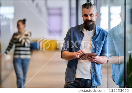 Bearded businessman standing in modern office hallway, holding digital tablet and looking confidently at camera, representing experience, leadership, and innovation in contemporary business 133353663