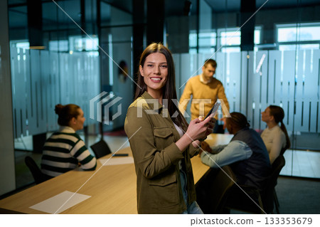 Confident business woman smiling while using smartphone during a team meeting in a modern office environment. Concept of communication, leadership, and professional confidence. 133353679