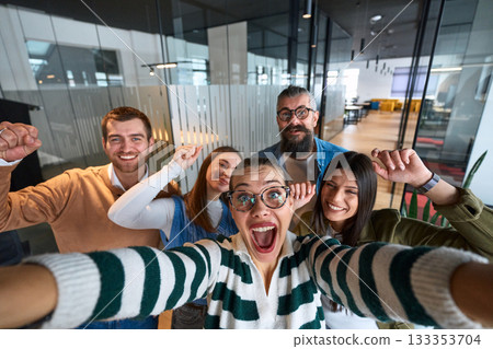 Group of cheerful coworkers taking a selfie together in a modern office environment. Concept of teamwork, friendship, success, and positive company culture. 133353704