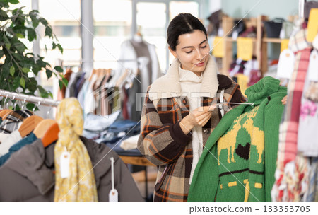 Girl chooses fashionable sweater in clothing store Girl chooses fashionable sweater in clothing store 133353705