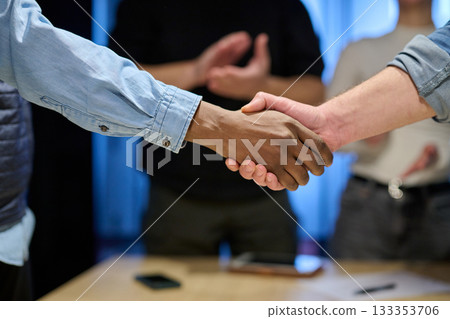 Two businessmen shaking hands after successful negotiation in a modern office, symbolizing partnership, agreement, success, and teamwork. A woman in the background applauds the deal. Two businessmen shaking hands after successful negotiation in a modern office, symbolizing partnership, agreement, success, and teamwork. A woman in the background applauds the deal. 133353706